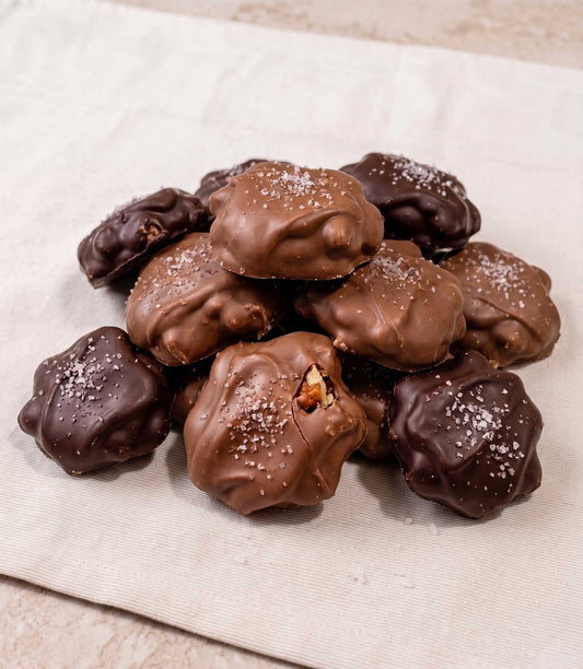 Hand-dipped caramel pecan clusters with sea salt in a white gift box